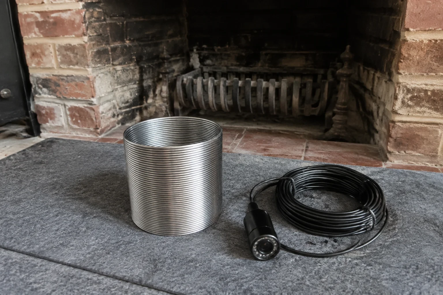 Detached metal liner section and camera equipment beside a fireplace.